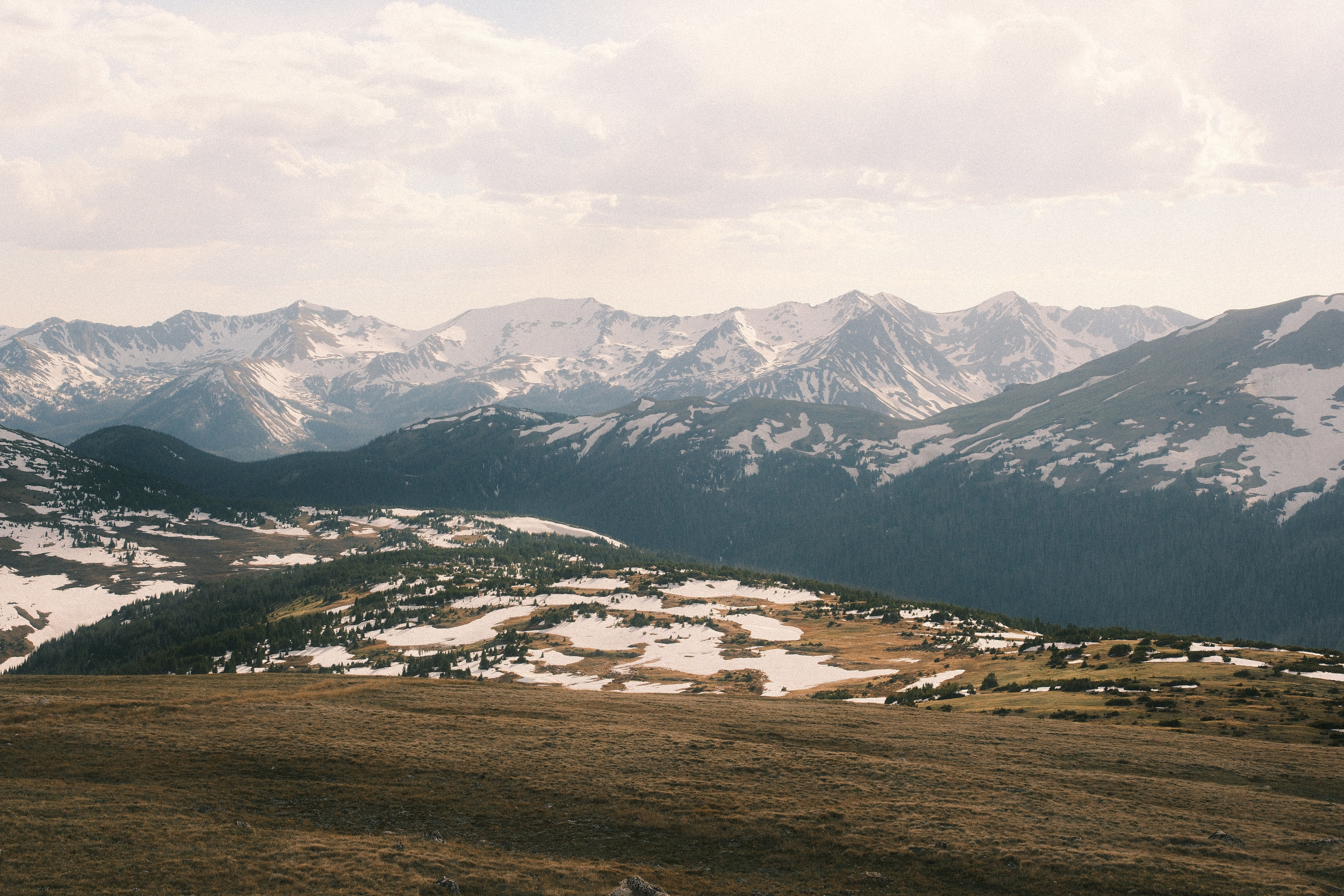 A sweep of alpine tundra falling away toward a distant range of snow-streaked peaks