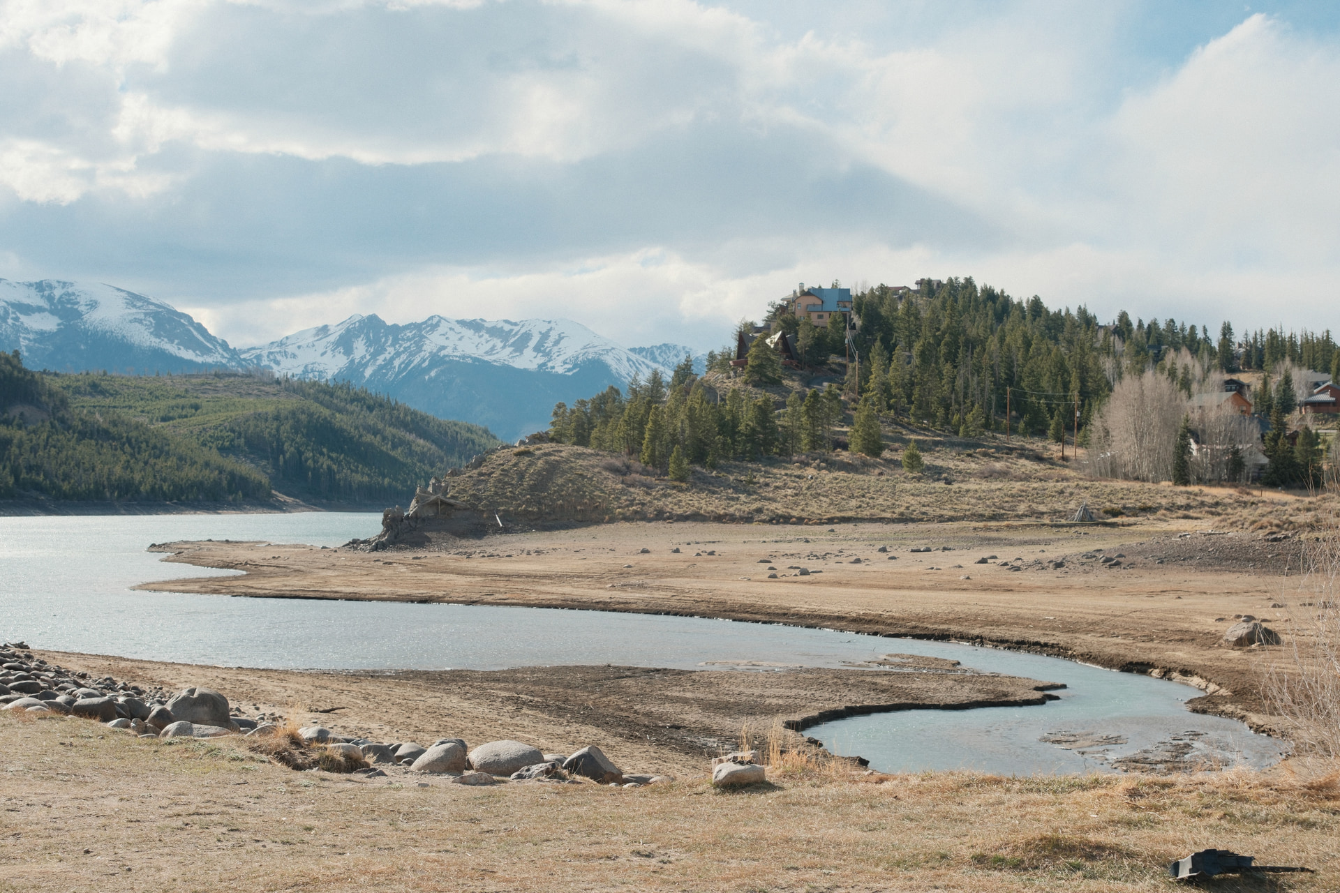 A reservoir with a low spring shoreline below snow-dusted peaks and evergreen hills