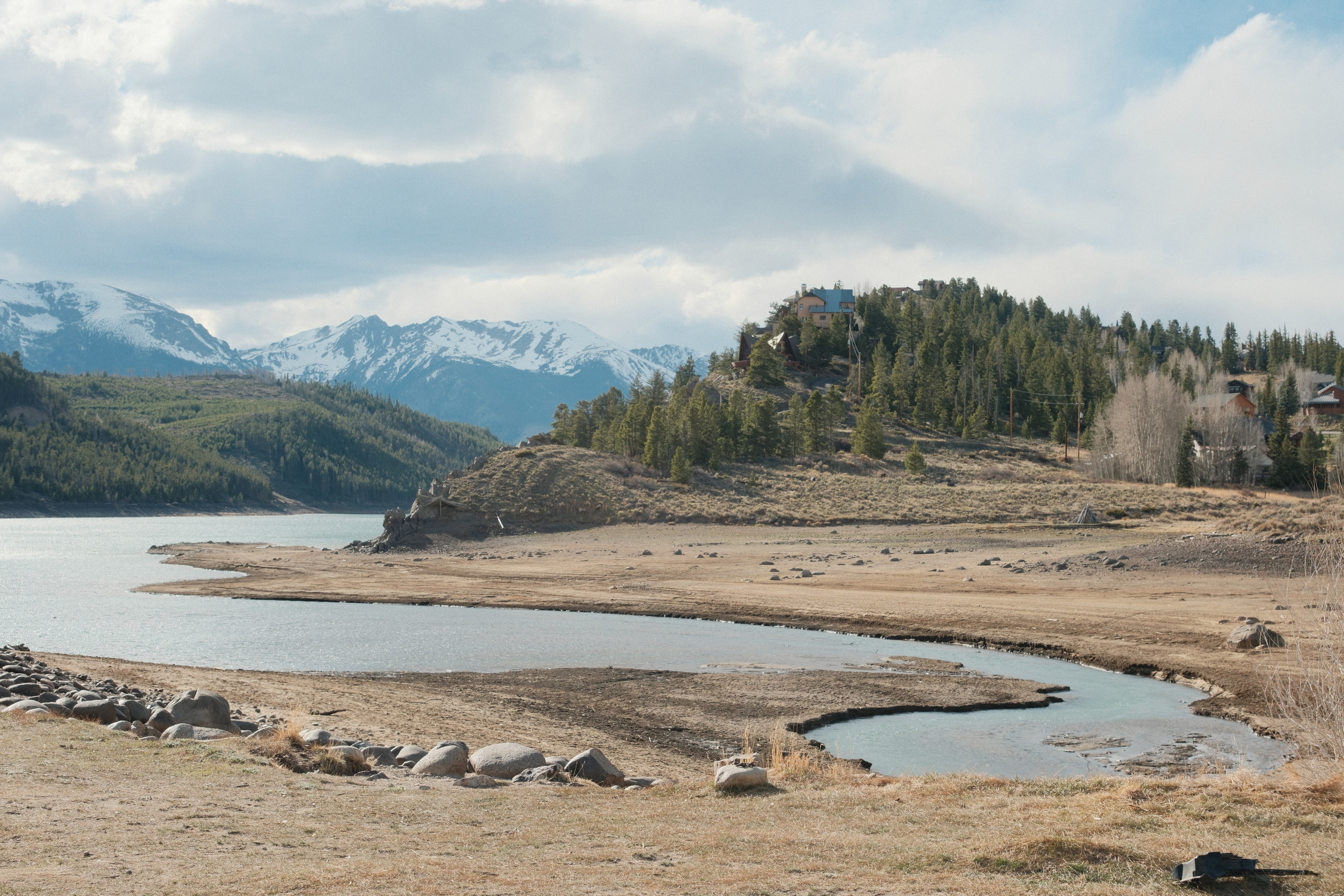 A reservoir with a low spring shoreline below snow-dusted peaks and evergreen hills